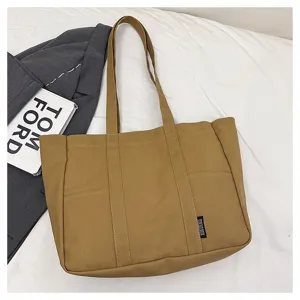 Canvas tote bag detail showing khaki fabric texture, dual shoulder straps, and front utility pocket.