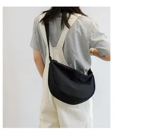 Detail view of a minimalist black nylon crossbody bag, casual crescent shoulder bag.