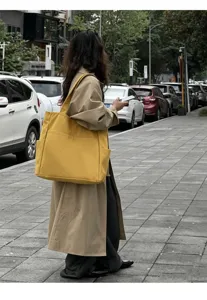 Detail shot of a large-capacity yellow canvas tote bag worn in a stylish street scene setting.