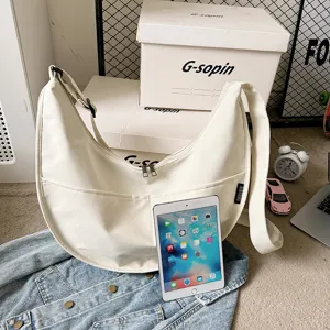 Detail view of solid color white dumpling shoulder bag with front pocket and adjustable strap.