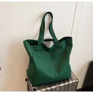 Detail shot of a dark green canvas tote bag placed on a silver suitcase, showing texture.