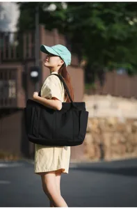 Outdoor street scene detail showing a black canvas tote bag with large capacity and pockets.