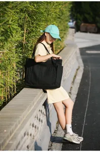 Detail view of large black canvas tote bag, stylish outdoor lifestyle shot with model.