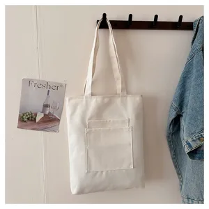 Detail shot of a minimalist white canvas shoulder tote bag featuring multiple front pockets.