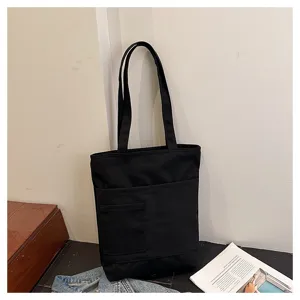 Detail view of black canvas tote bag with front pocket, showcasing everyday casual design.