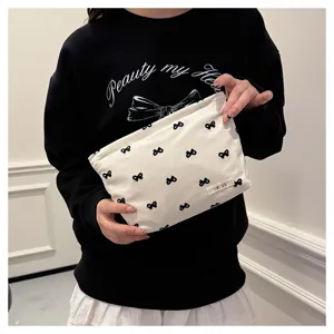 Detailed shot of a cute white canvas cosmetic bag featuring small black bow patterns for daily use.