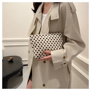 Detailed shot of woman holding a chic black and white polka dot makeup bag and clutch.