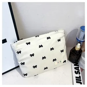 White canvas cosmetic bag with cute black bow pattern, portable travel makeup pouch for women.