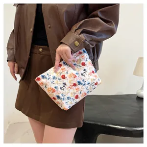 Close-up detail of white 3D floral embroidered cosmetic bag held by model, elegant style.
