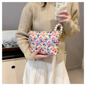 Close-up detail of a trendy cosmetic bag featuring colorful 3D rose print and chic pearl wrist strap.