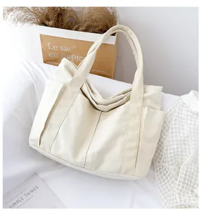 Canvas tote bag detail showing large capacity, front pockets and double handles in off-white.