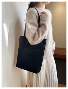 Black canvas tote bag detail view, casual shoulder bag with outer pocket and zipper closure.