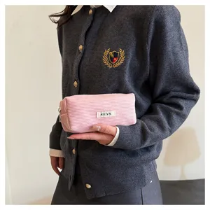 Detailopname van het roze corduroy etui met fijne textuur en een klein merklabel.