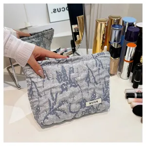 Detail view of grey crinkled cosmetic pouch with cross pattern texture and brand label.