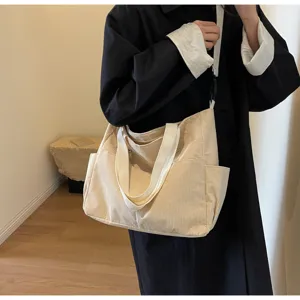 Detail shot of a casual beige corduroy shoulder tote bag with white straps and side pockets.