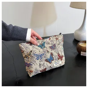 Detailed view of a stylish woven tapestry makeup pouch with butterfly print, held by hand.