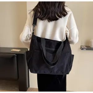 Black corduroy shoulder tote bag worn in indoor lifestyle setting, casual commute style.