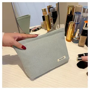 Detailed shot of light green corduroy cosmetic bag on dressing table with brushes.