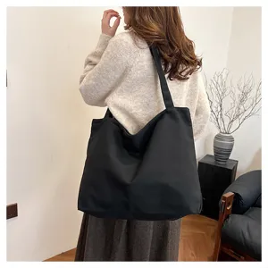 Detail view of a stylish black canvas tote bag worn by a model, showing large capacity.