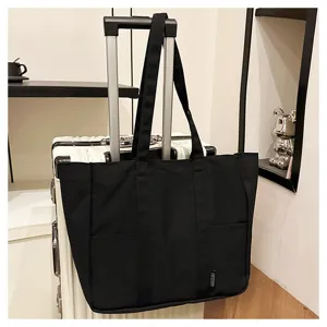 Detailed view of black canvas tote bag hanging on suitcase handle, casual style, spacious capacity.