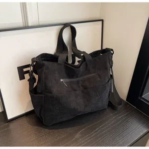 Detail view of black corduroy tote bag showing front zipper pocket and shoulder strap.