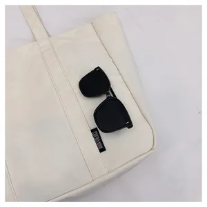 Close-up detail of off-white canvas tote bag featuring front pocket and casual daily style.