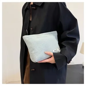 Light blue corduroy cosmetic pouch detail, soft textured fabric clutch bag with label.