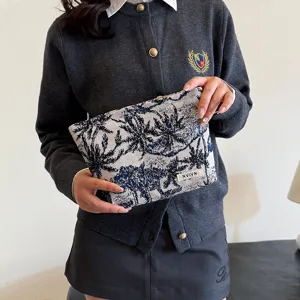 Vue détaillée d'une trousse de maquillage chic avec imprimé palmiers et étiquette tissée.