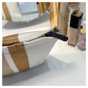 Striped canvas cosmetic bag detail view showing fine linen texture and black zipper pull.