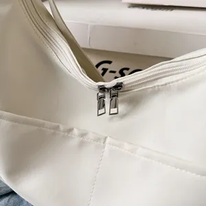 Close-up detail of white shoulder dumpling bag, showing smooth double zippers and front pocket.