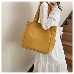 Detail view of a yellow canvas tote bag worn on shoulder by model near wooden stairs.