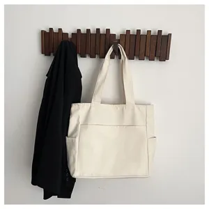 Detail view of large cream canvas tote bag with functional pockets hanging on wooden rack.