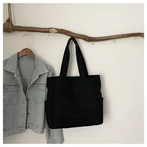Detailed view of black canvas tote bag hanging on wooden branch with denim jacket.