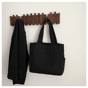 Detail shot of a black canvas tote bag hanging on a stylish wooden wall rack in a clean room.