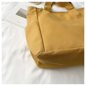 Detail shot of yellow canvas tote bag showing fine fabric texture and neat stitching construction.
