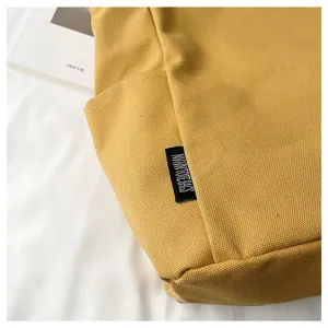 Close-up of yellow canvas tote bag detail, featuring durable fabric and woven label.