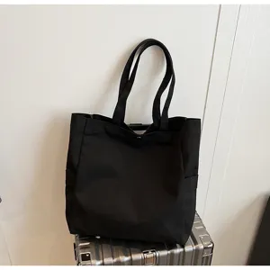 Detailed view of a minimalist black canvas tote bag with comfortable shoulder straps and side pockets.