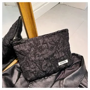 Close-up detail of black crinkled fabric texture clutch cosmetic bag with white label.