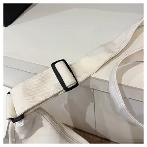 Gros plan détaillé de la bandoulière réglable d'un sac en toile blanche avec boucle.