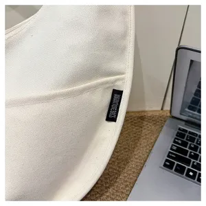 Vue détaillée du sac dumpling en toile blanche, sac bandoulière minimaliste et décontracté.