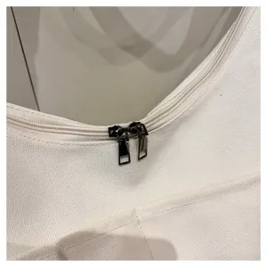 Gros plan détaillé d'un sac bandoulière en toile blanche avec fermetures éclair métalliques.