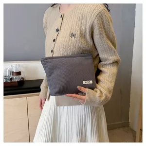 Detailed view of a solid gray corduroy makeup pouch held in hand for daily storage.