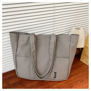 Close-up detail of a grey canvas tote bag with front pockets and sturdy handles on a wooden table.