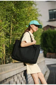 Detail view of large black canvas tote bag with multiple pockets, outdoor lifestyle scene.