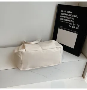 Detailed view of a solid off-white quilted shoulder tote bag in a minimalist setting.