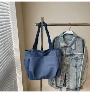 Detail shot of the blue solid color shoulder tote bag hanging on a rack with denim jacket.