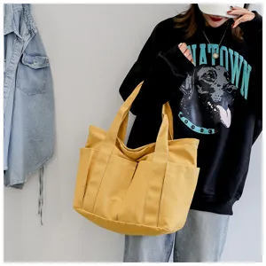 Detailed view of the yellow canvas tote bag featuring multiple exterior utility pockets.
