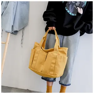 Detailed view of the yellow canvas tote bag showing multiple practical outer pockets and straps.