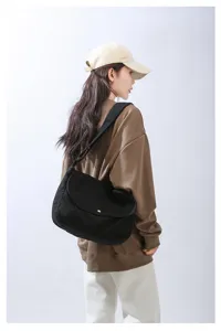 Close-up view of black canvas shoulder bag showing minimalist flap and adjustable wide strap.
