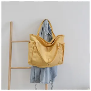 Detailed shot of yellow canvas tote bag hanging on wooden ladder with denim shirt design.